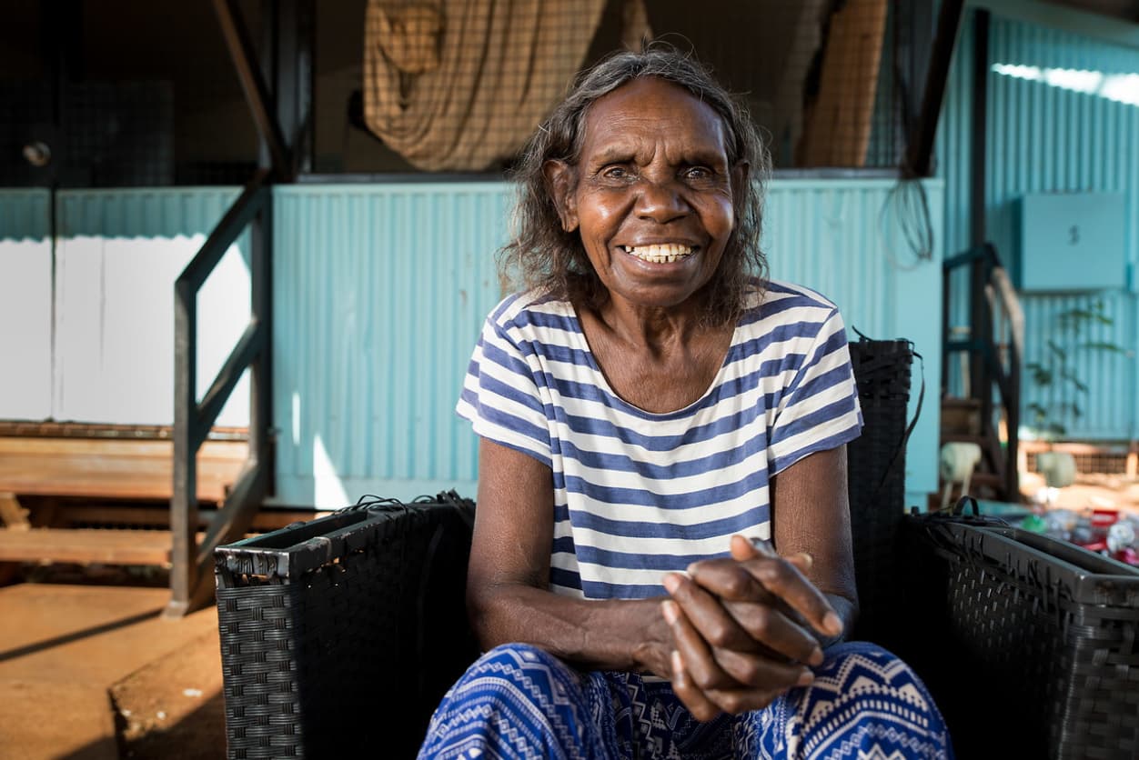 A woman sitting on a chair with her elbows resting on her legs, and her hands clasped together.