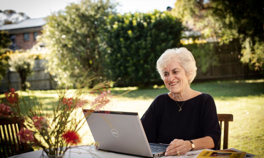 Older woman sitting outside at a table in front of a laptop