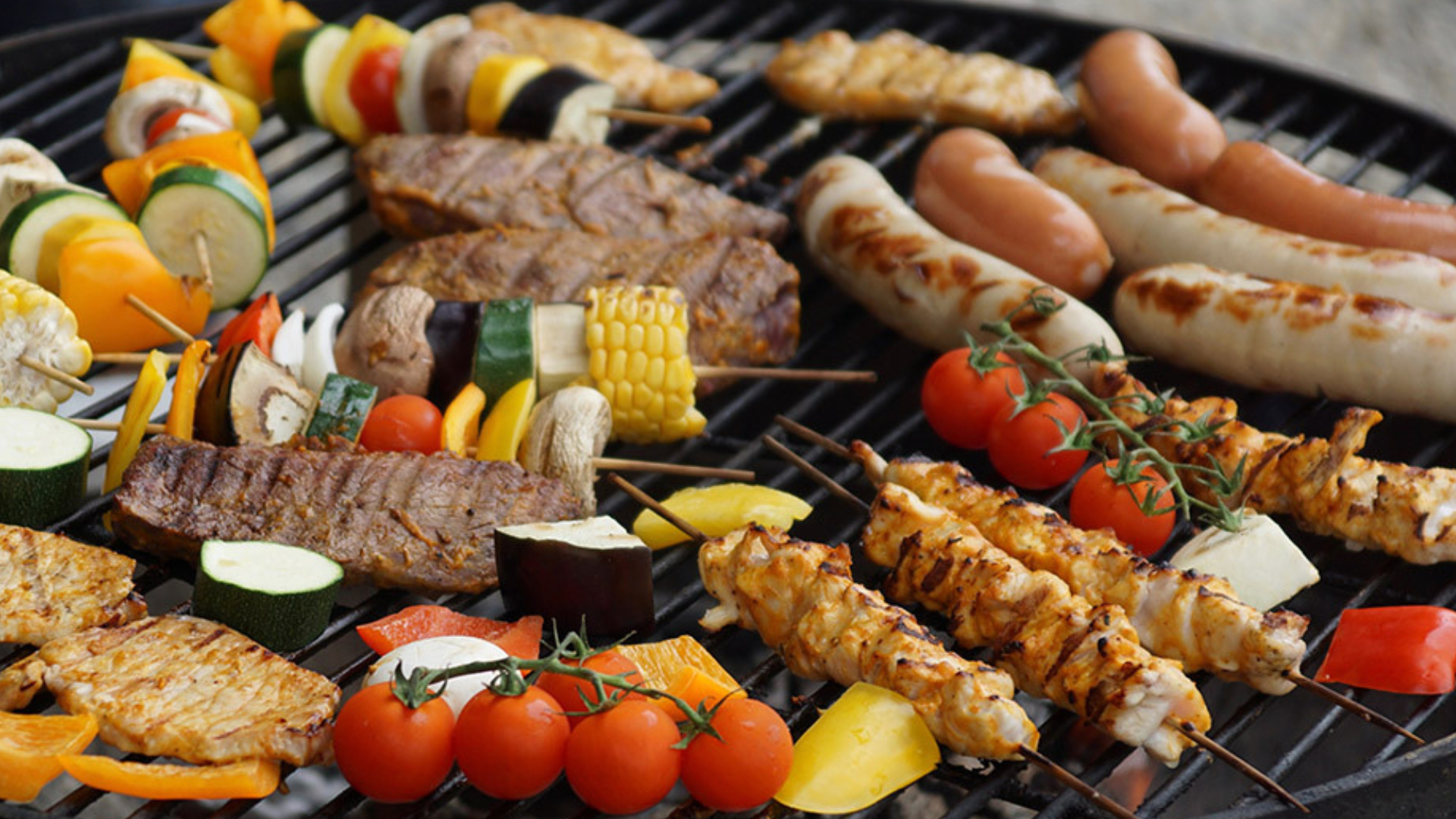 An image of a BBQ cooking sausages, corn and vegetables