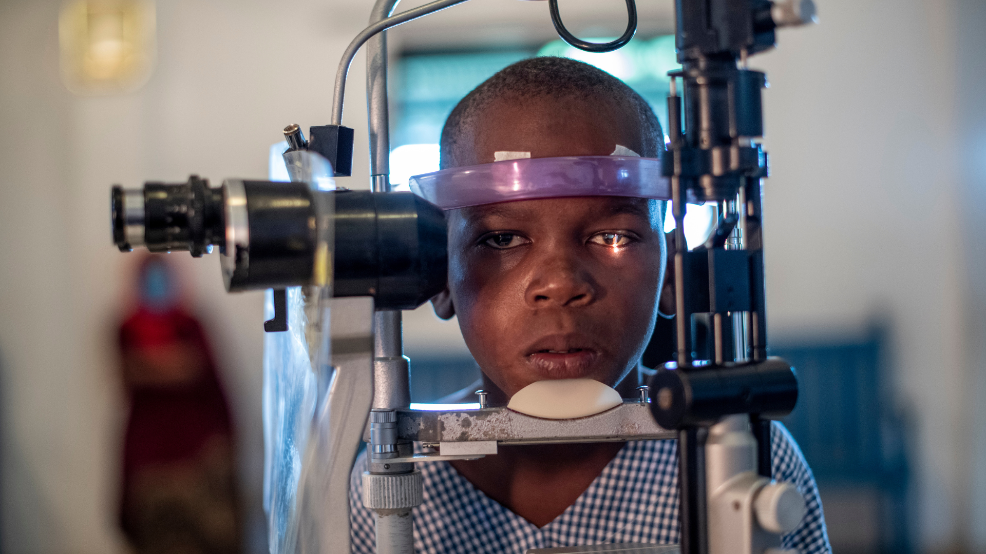 Mbaruku resting his chin on the eye screening equipment as he goes through he screening process