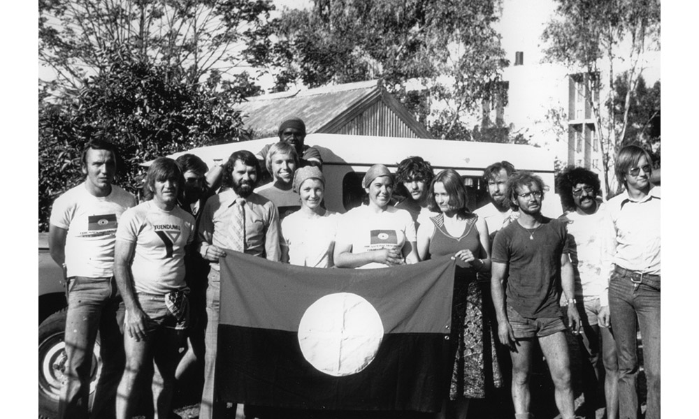 Fred Hollows with a group standing in front of the Aboriginal flag 