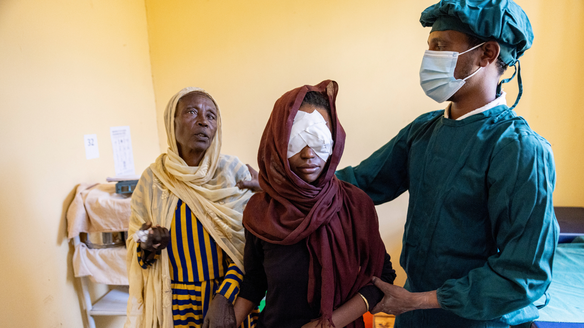 Semira with her mother in law walking through a hospital with her eye patches on