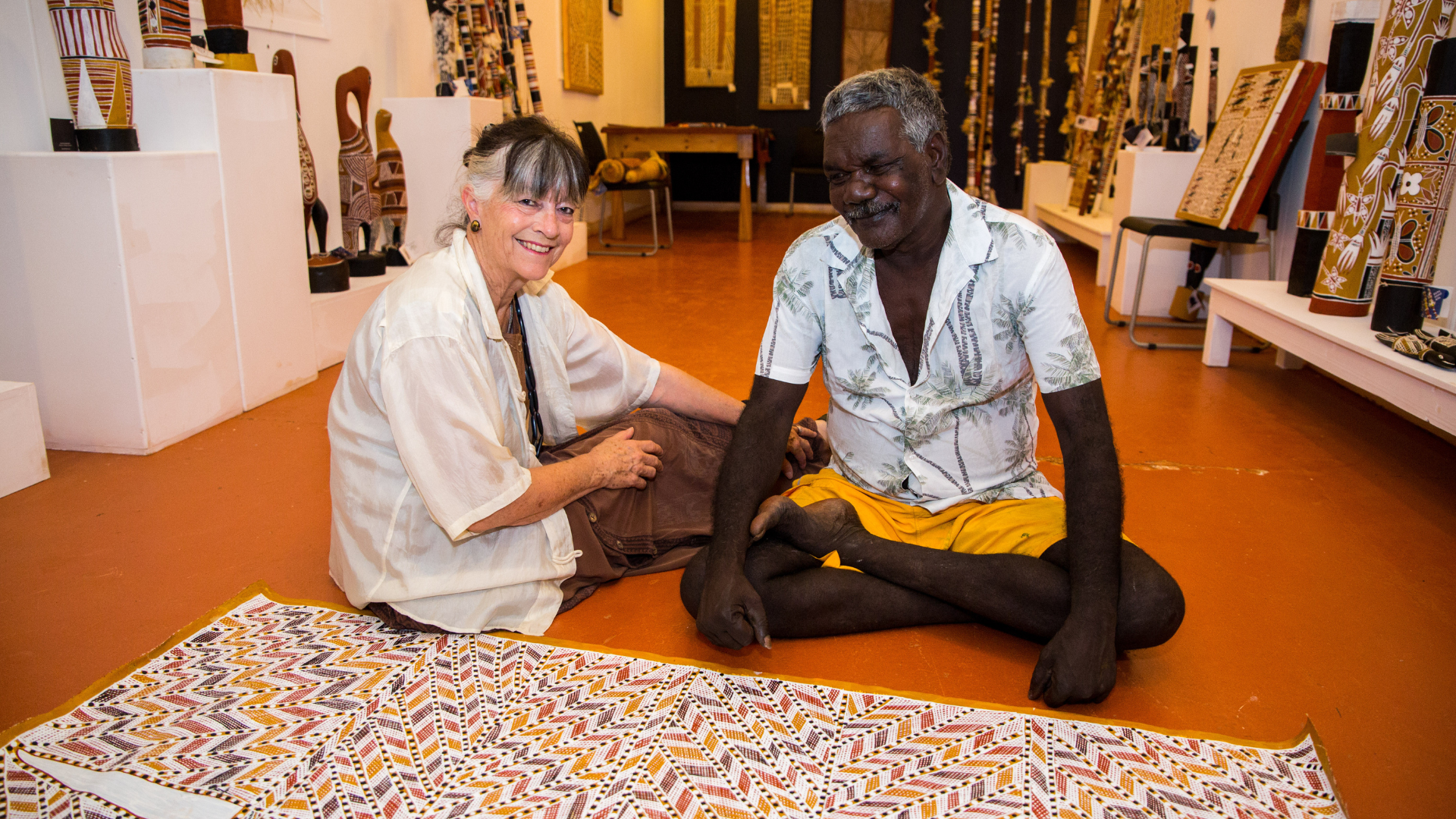 Gabi Hollows and Long John sitting the floor looking over Long John's artwork in the foreground