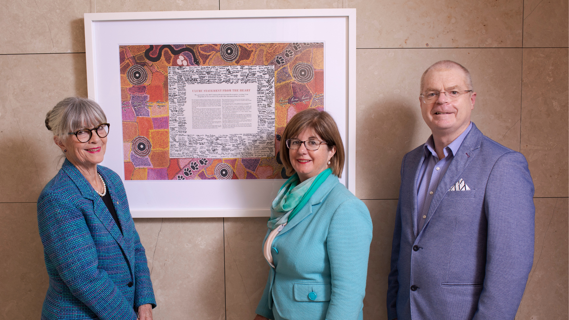 Board members Gabi Hollows, Jane Madden and Ian Wishart standing in front of a frame of the Uluru Statement from the Heart 