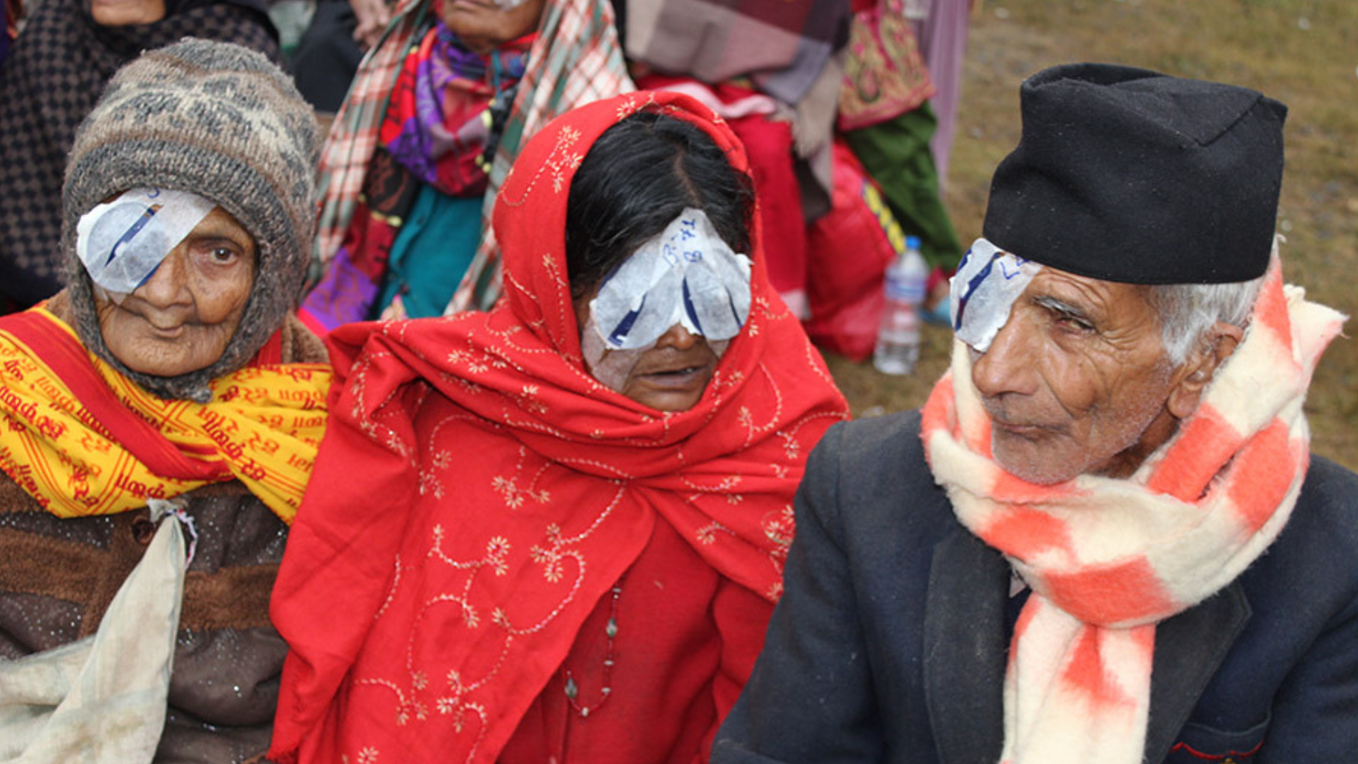 Three people in Nepal pictured sitting side by side together, waiting to take their eye patches off after surgery