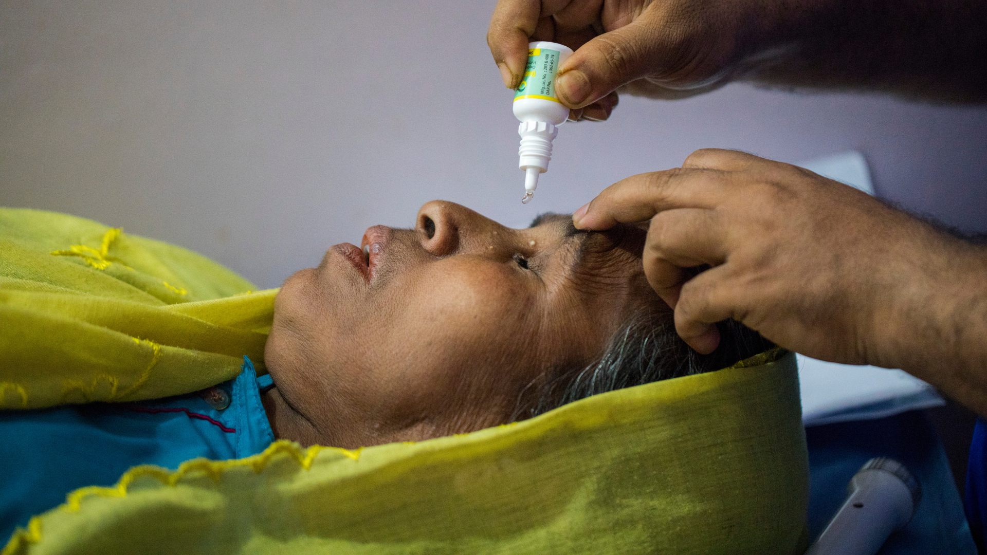 A woman from Bangladesh lying down, getting eye drops put in her eyes 