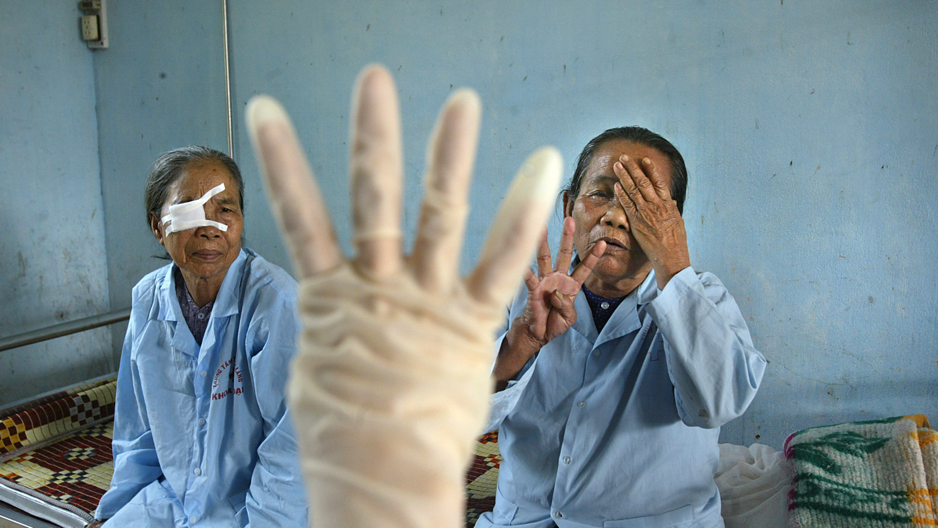 Two Vietnamese women sitting on a bed, getting their eyes tested