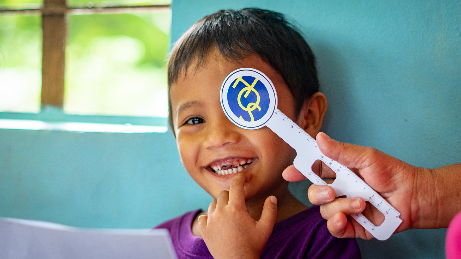 A boy from the Philippines looking at the camera and smiling while he gets his eyes examined