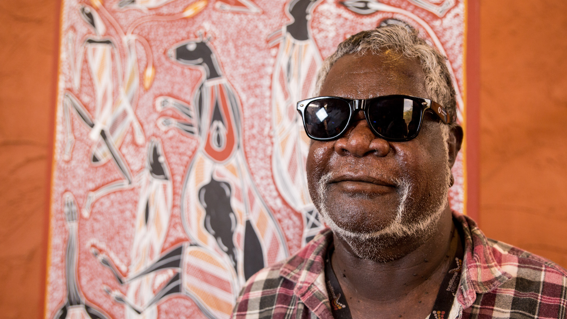 Long John standing in front of his artwork smiling with sunglasses on