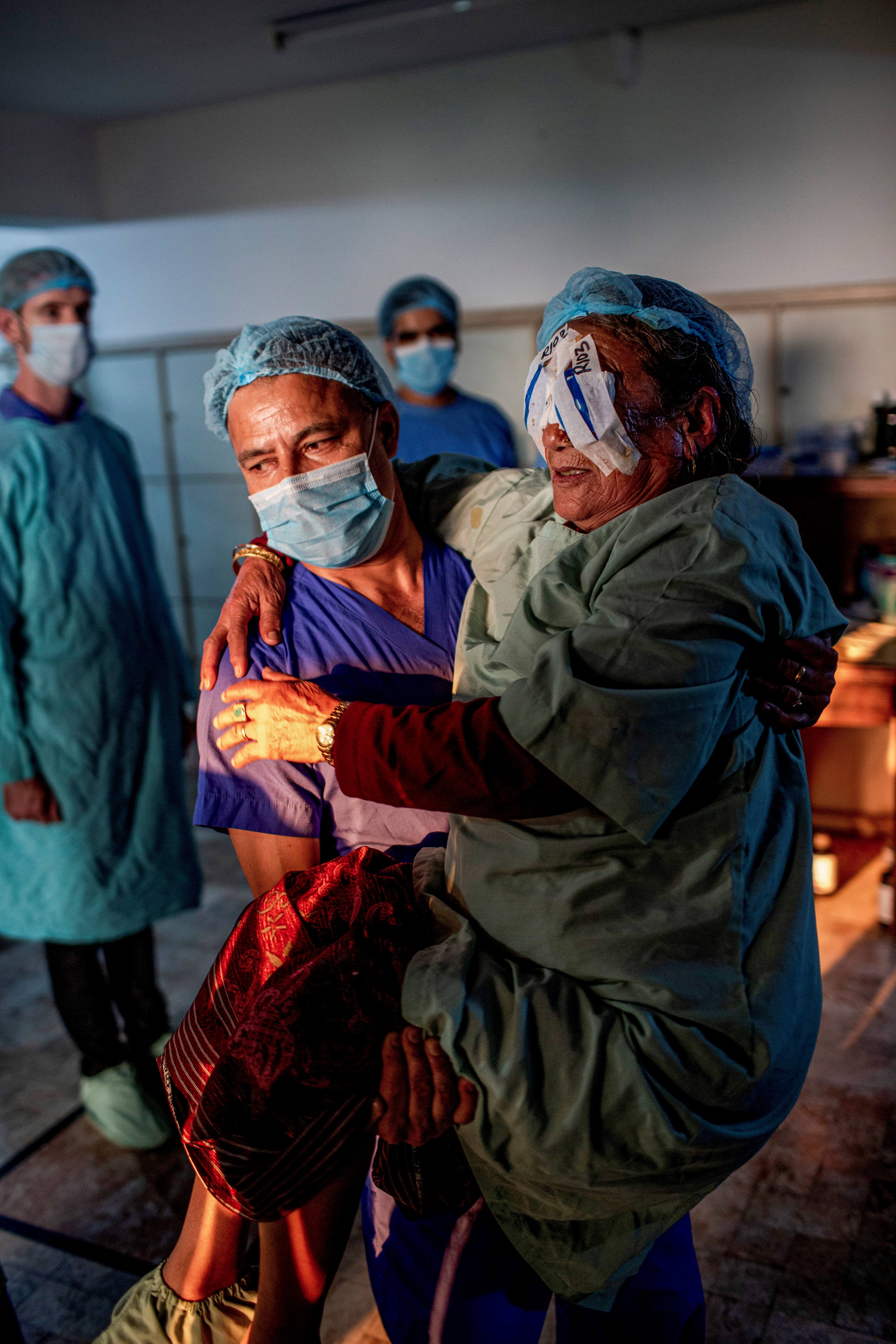 Pictured: bilaterally blind Chini Lama, 74, on the outskirts of Kathmandu. Ophthalmic Assistant Pradeep Karki carries Chini after her cataract surgery at the Pullahari Eye Camp. Photo taken by Michael Amendolia.