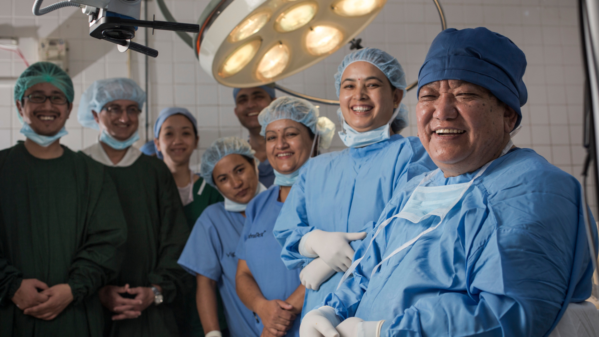 Dr Sanduk Ruit in scrubs with other surgeons in a surgical ward posing for the camera