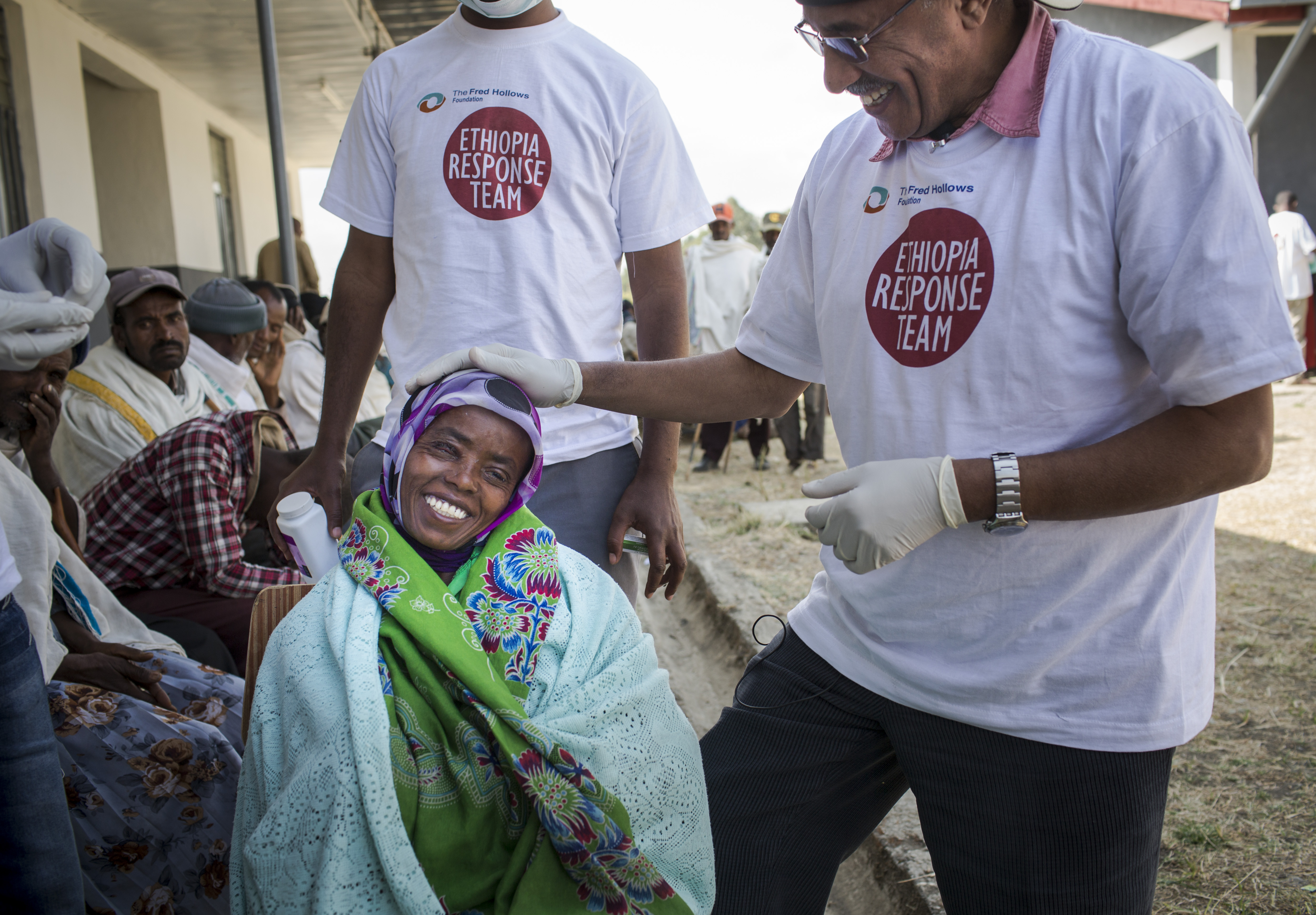 Shashetu smiling wide after her surgery while two Outreach Health Workers check on her