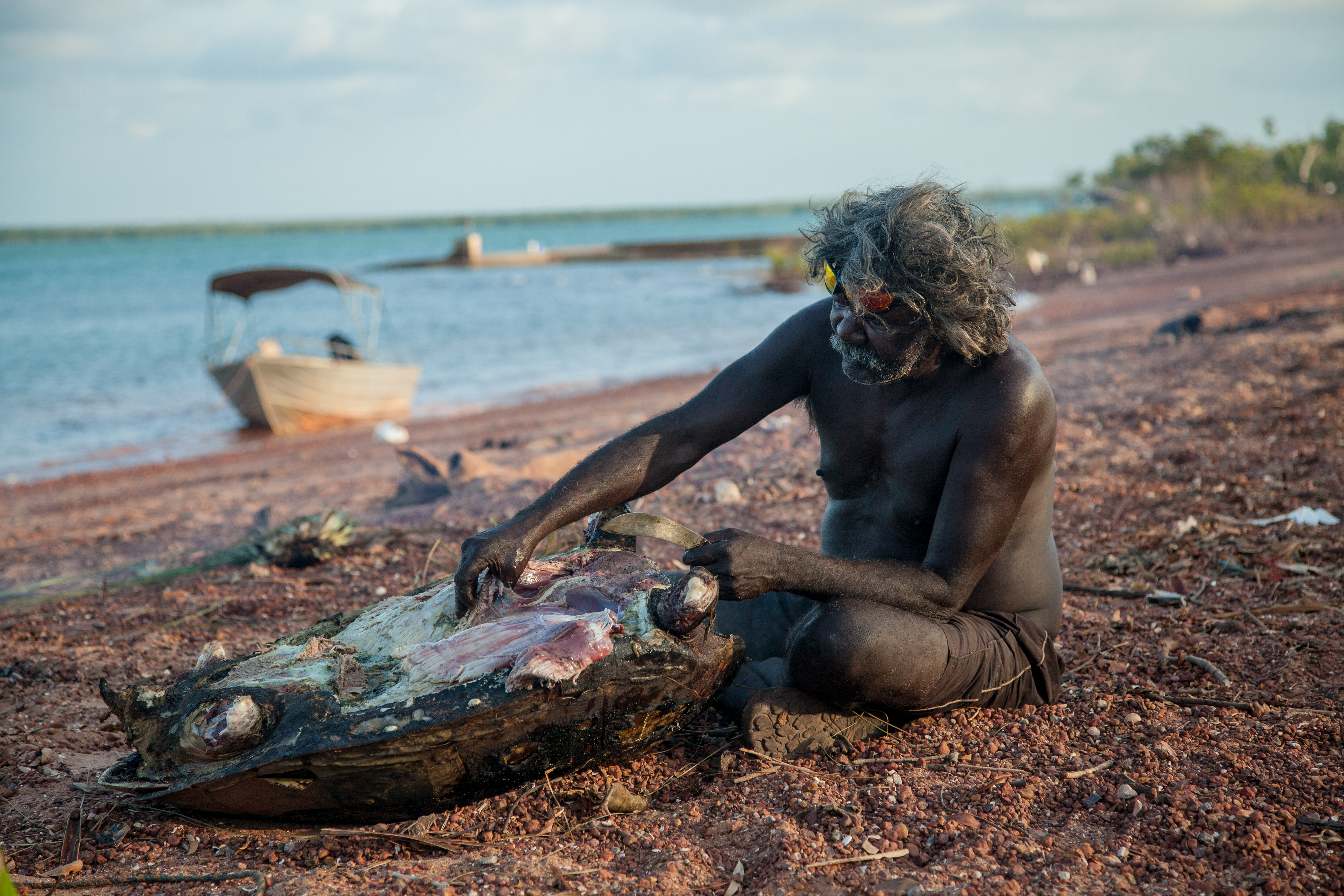 Peter sitting by the water, pulling meat off an animal