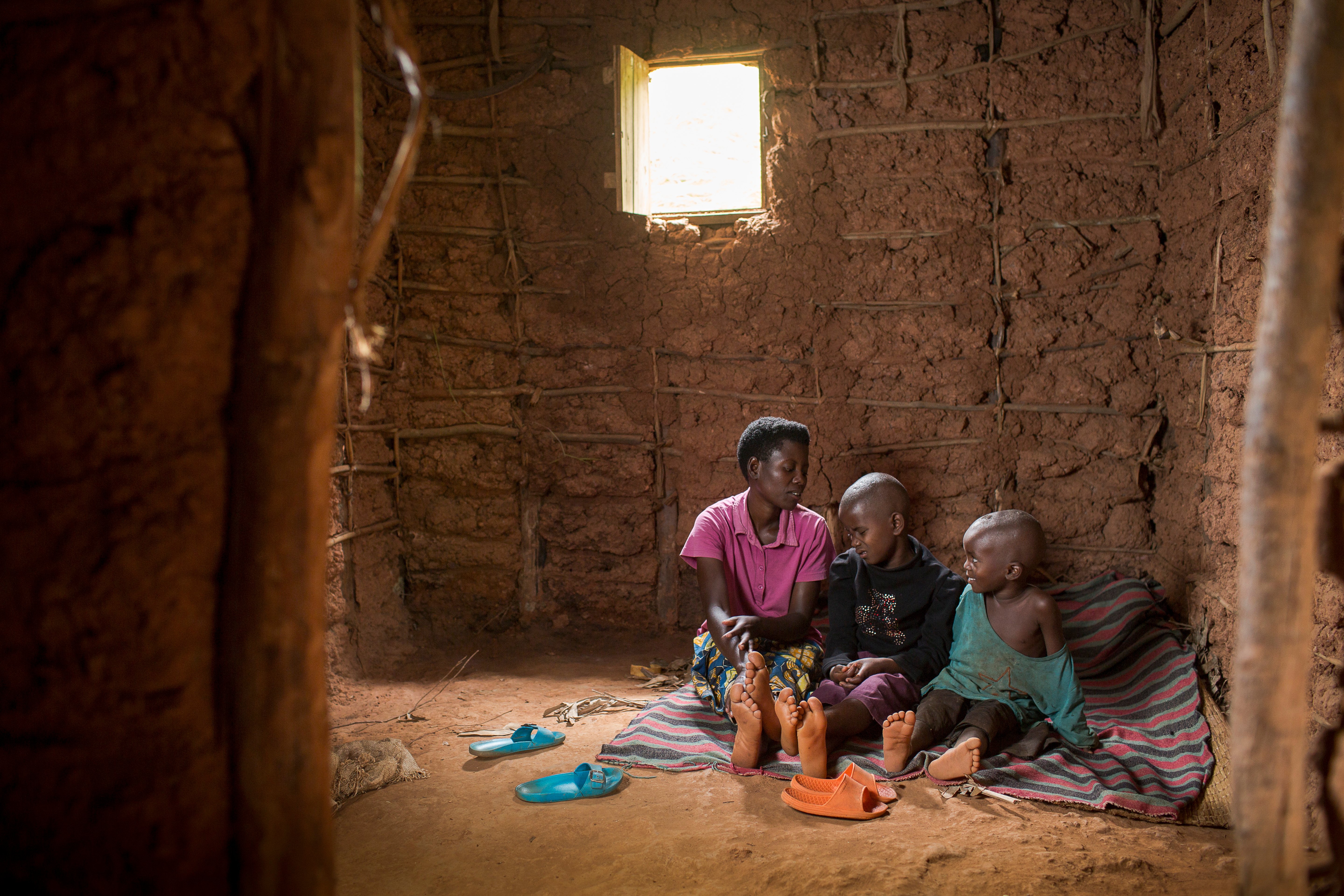 Eric sitting on a blanket on the ground of their house with his mother and brother by his side