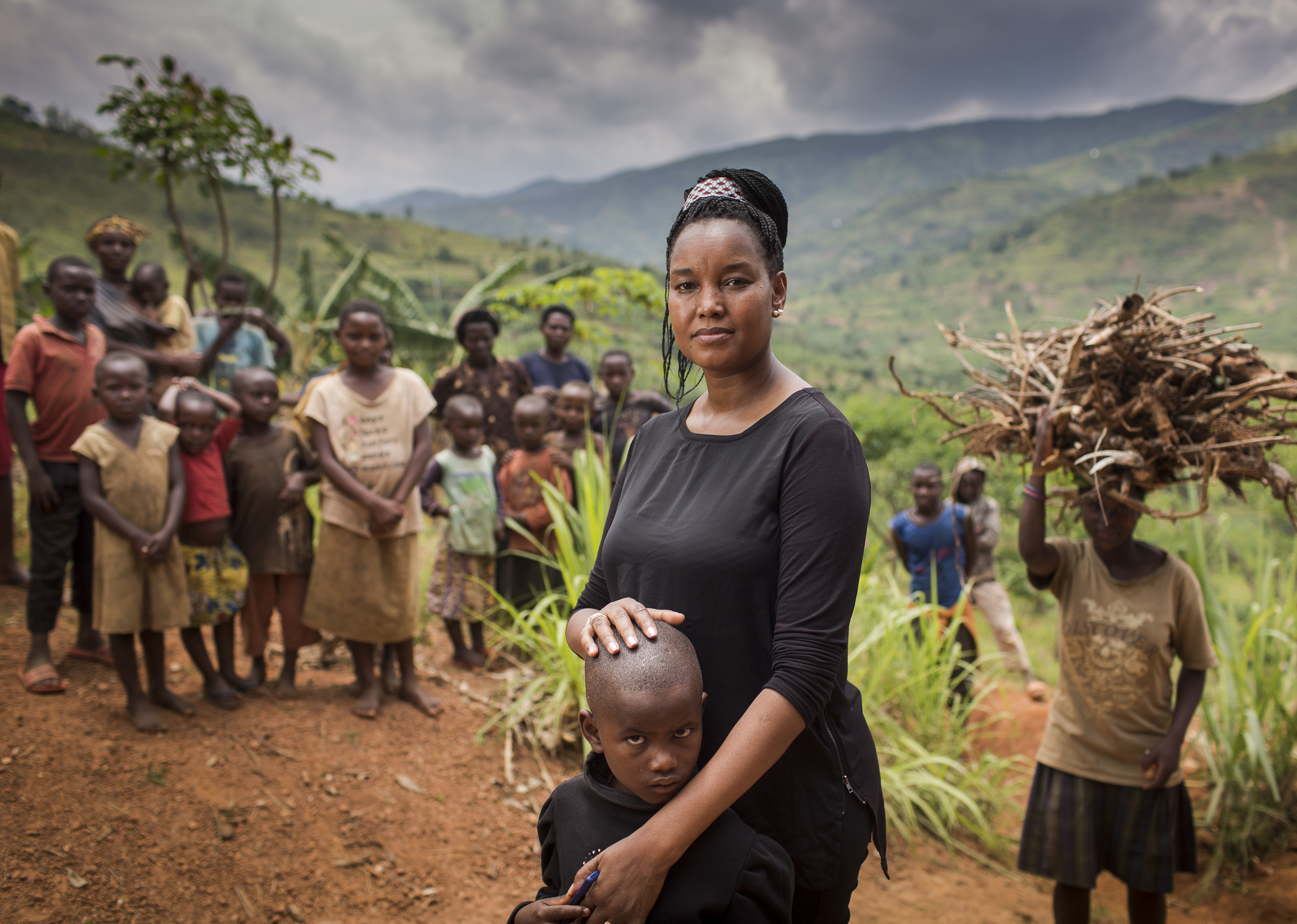 Dr Ciku (Wanjiku) Mathenge posing for the camera with her arms around Eric, and the community from Rwanda in the background