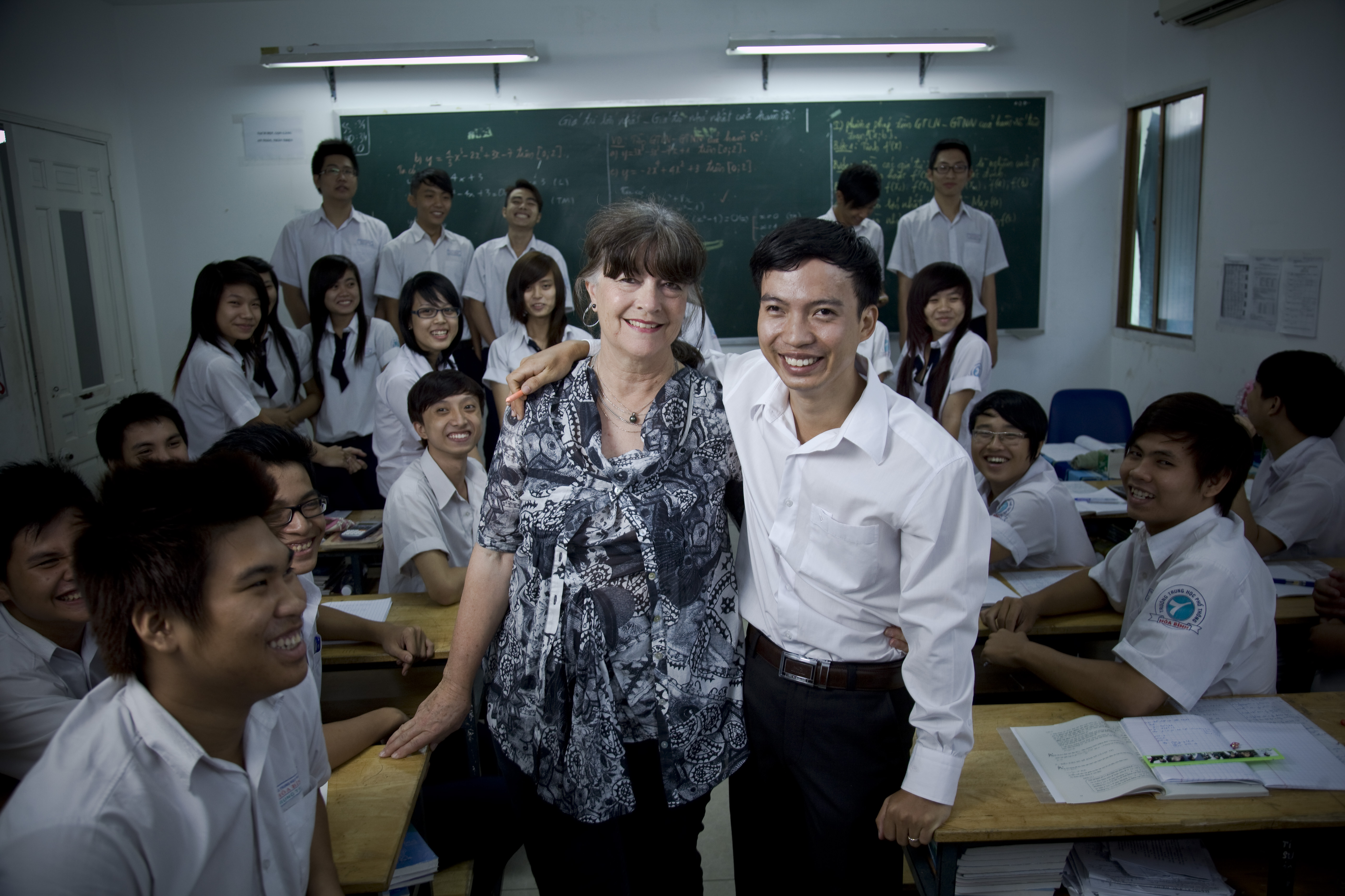 Giap and Gabi Hollows posing at the school Giap teaches, posing for the camera with arms around each other. Giap's students are smiling in the background